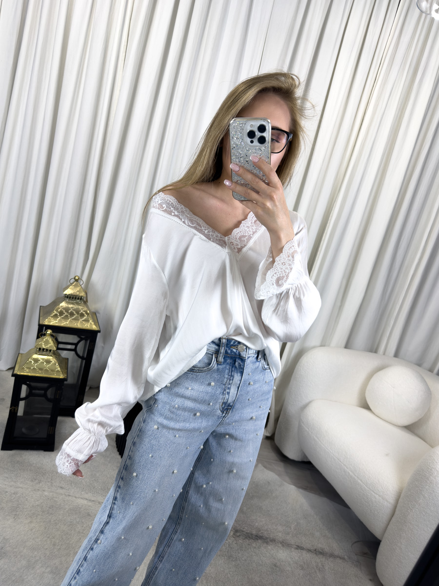 Bluzka satynowa Chic biała z koronkowym dekoltem w literę V oraz bufiaste rękawy z koronką, zestawiona z jeansami z perełkami – stylizacja łącząca elegancję z codziennym luzem.