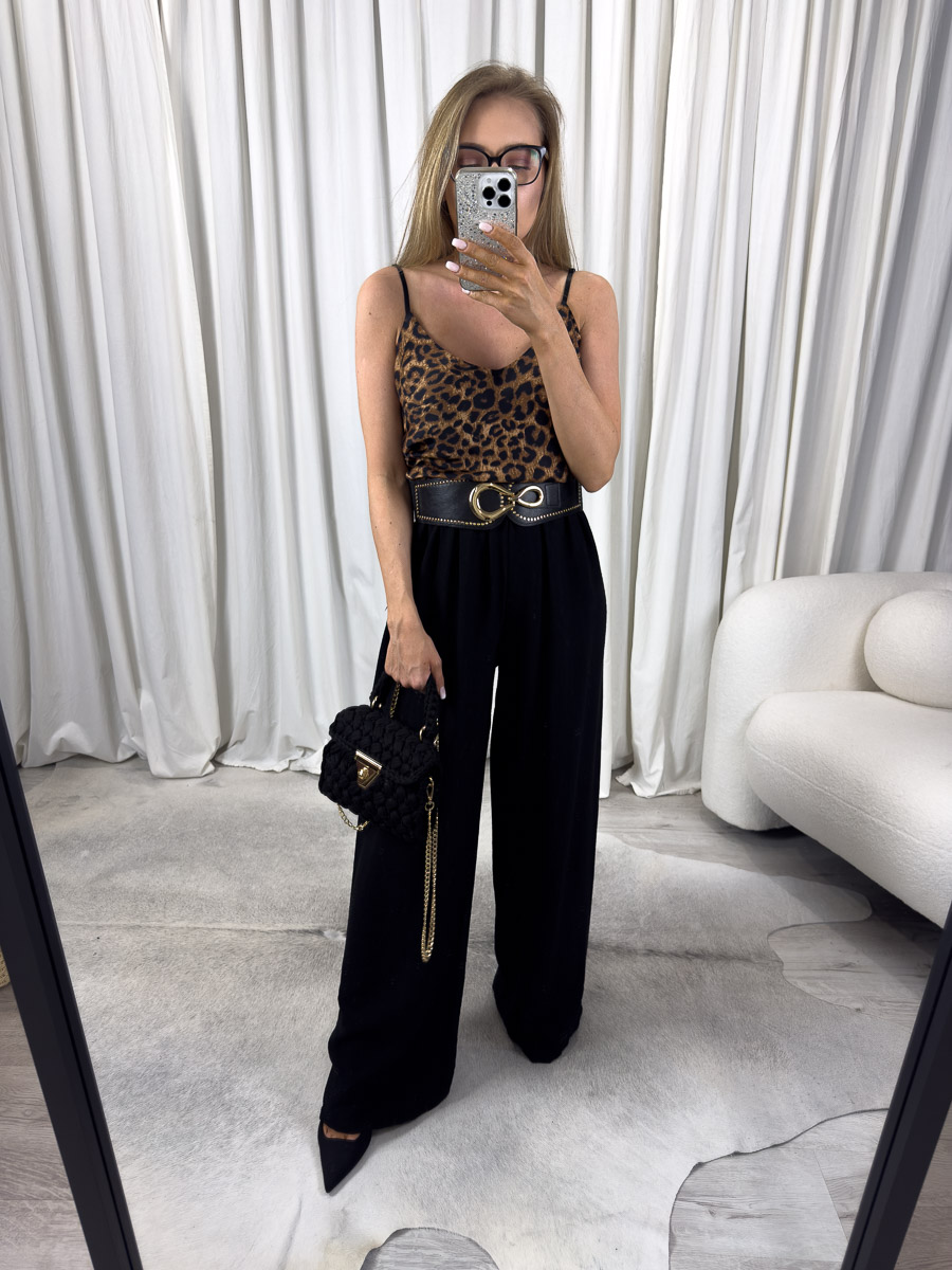 Zdjęcie produktowe sklepu internetowego z odzieżą damską – modelka ubrana w top satynowy Animal Print, czarne spodnie palazzo, trzymająca w ręce małą czarną torebkę