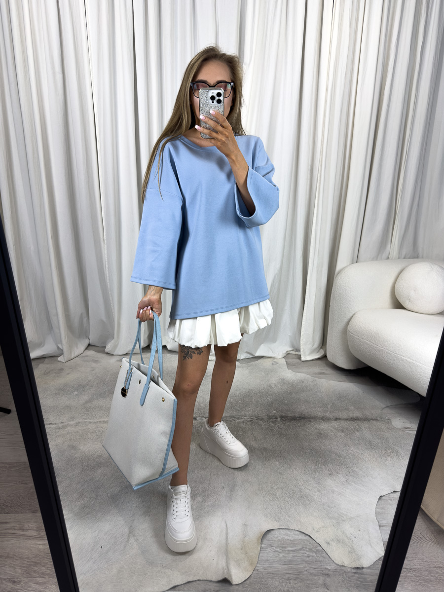 Modelka w bluzie oversize Basic błękitnej i białej spódniczce, z jasną torbą i białymi sneakersami – stylizacja pastelowa na co dzień.