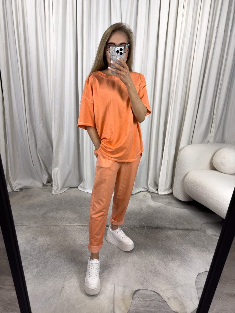 Modelka ubrana w pomarańczowy komplet dresowy Skinny Wiya oraz białe sneakersy.