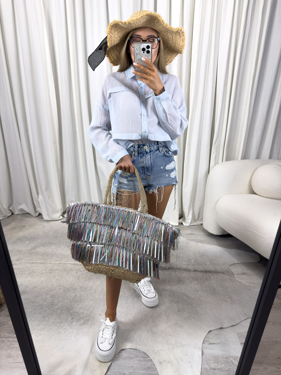 Zdjęcie produktowe sklepu internetowego z odzieżą damską – modelka w błękitnej koszuli minimalistycznej Flash Gioya, szortach jeansowych, kapeluszu i z torbą na ramieniu.