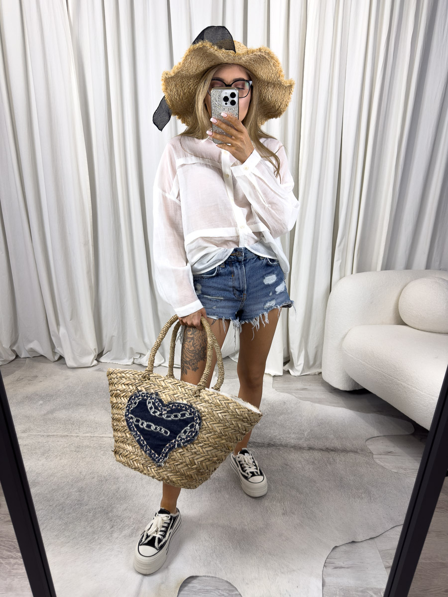 Zdjęcie produktowe sklepu internetowego z odzieżą damską – modelka w jasnej koszuli minimalistycznej Flash Gioya, szortach jeansowych, kapeluszu i z wiklinową torbą z sercem z dżinsu