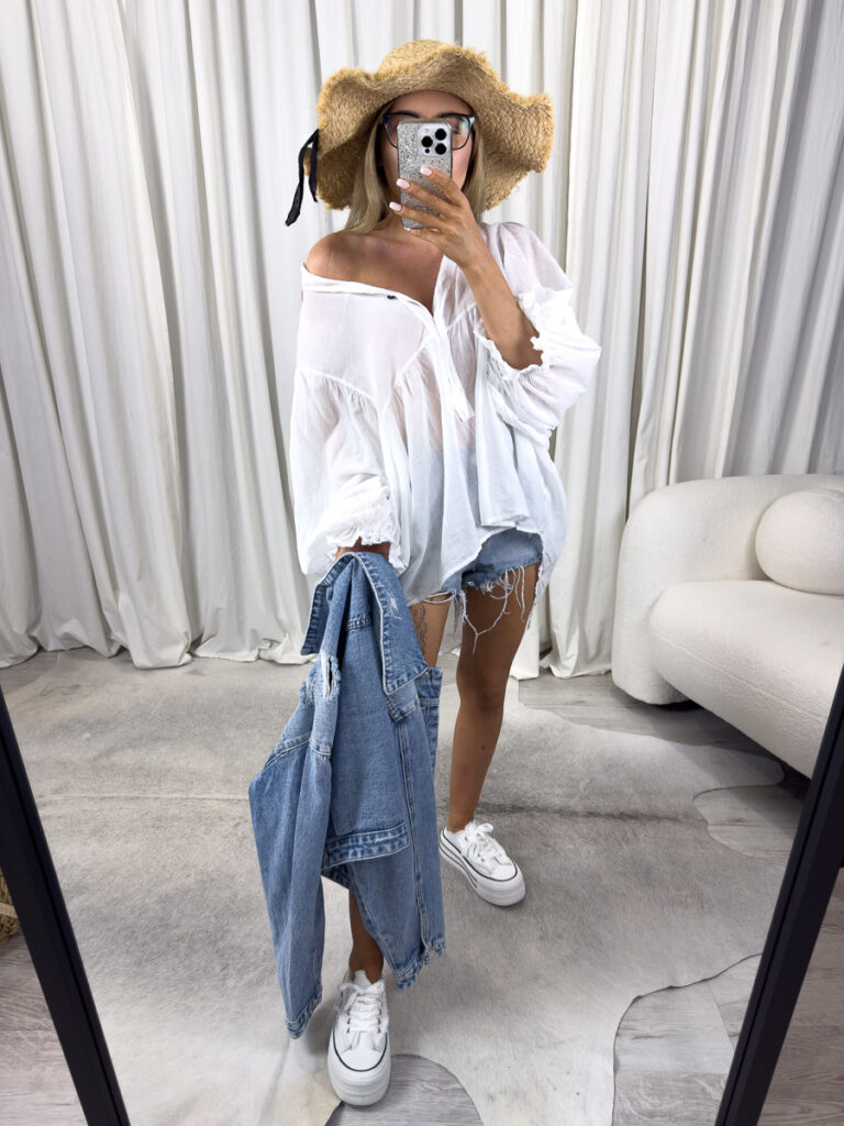 Zdjęcie produktowe sklepu internetowego z odzieżą damską – modelka w lekkiej koszuli Sand, jeansowych szortach, z kapeluszem.