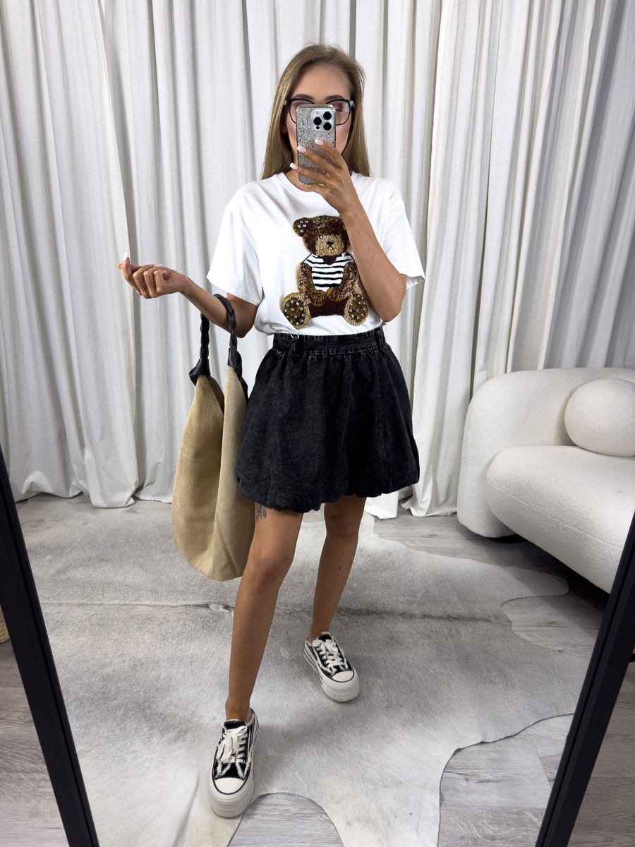 Zdjęcie produktowe sklepu internetowego z odzieżą damską – modelka w trampkach ubrana w t-shirt Teddy biały, spódnicę w kolorze dekatyzowanej czerni trzymająca w ręce zamszową torebkę