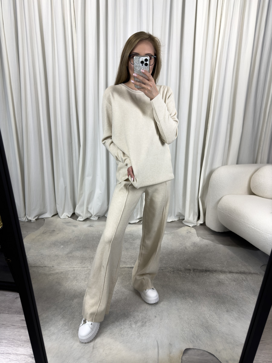 Komplet dzianinowy Comfy kremowy – luźna bluza i proste spodnie, stylizacja z białymi sneakersami na tle jasnego wnętrza.
