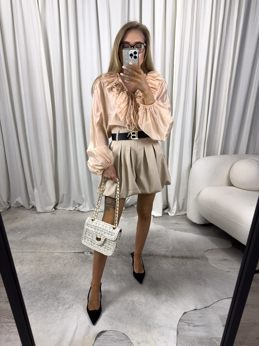 Zdjęcie produktowe sklepu internetowego z odzieżą damską – modelka ubrana w koszule Caroline w kolorze morelowym marki Miho’s, beżowe spódnico-spodenki, trzymająca w ręce małą kremową torebkę