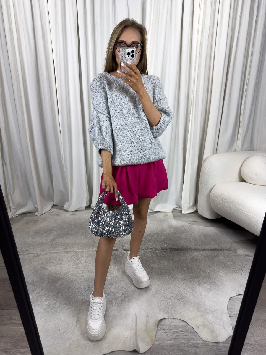 Kobieta w szarym swetrze Fluffy, fuksjowej spódnicy i białych sneakersach, trzymająca cekinową torebkę – miejska stylizacja z nutą glamour
