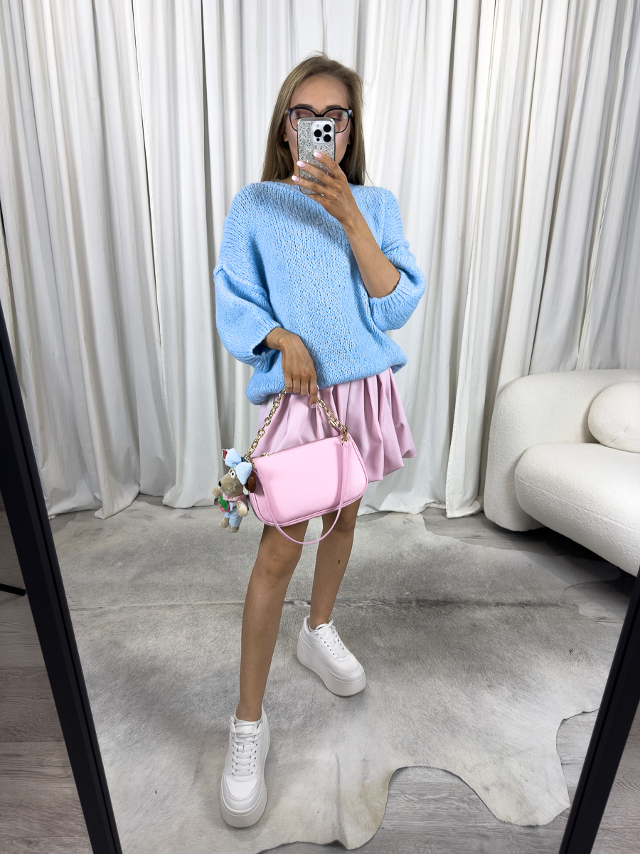 Kobieta w błękitnym swetrze wiosennym Fluffy, różowej spódniczce i białych sneakersach, trzymająca różową torebkę – stylizacja soft girl na wiosnę