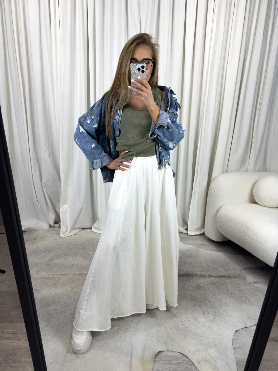 Modelka prezentuje luźne spodnie Baggy Wiya w kremowym kolorze z szerokimi, zwiewnymi nogawkami i wysokim stanem, zestawione z oliwkowym topem i kurtką jeansową z gwiazdkami, w stylizacji casual, na tle jasnych zasłon.