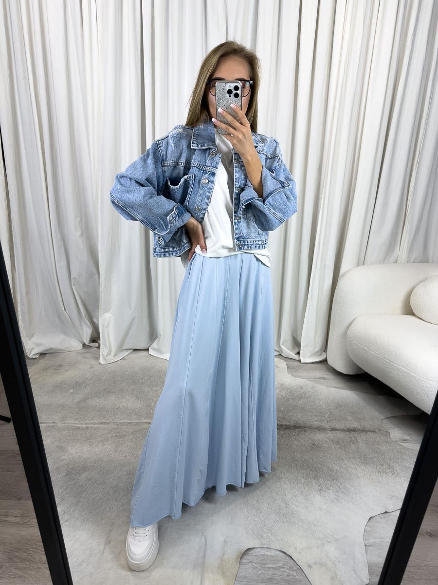 Modelka prezentuje luźne spodnie Baggy Wiya w odcieniu błękitnym z szerokimi, zwiewnymi nogawkami i wysokim stanem, zestawione z białym T-shirtem i kurtką jeansową, w lekkiej stylizacji casualowej, na tle jasnych zasłon.