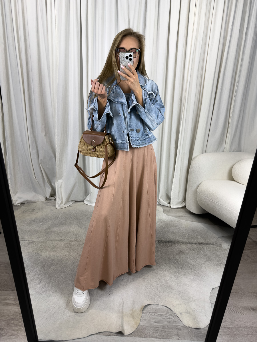 Modelka prezentuje luźne spodnie Baggy Wiya w odcieniu morelowym z szerokimi, zwiewnymi nogawkami i wysokim stanem, zestawione z kurtką jeansową, w lekkiej stylizacji casualowej, na tle jasnych zasłon.