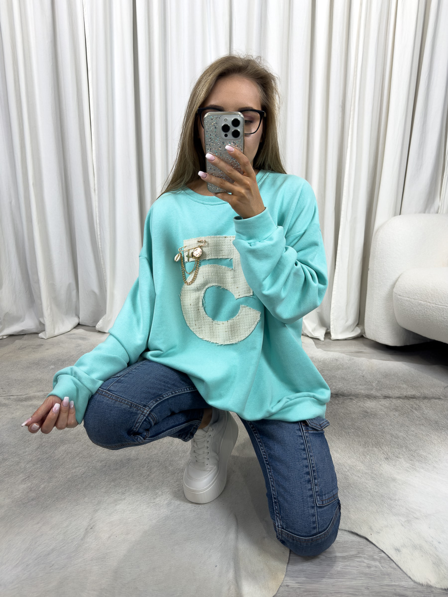 Bluza oversize Five turkusowa z dużą cyfrą 5 i ozdobą, stylizacja z jeansami i białymi sneakersami, zdjęcie produktowe na tle jasnych zasłon.