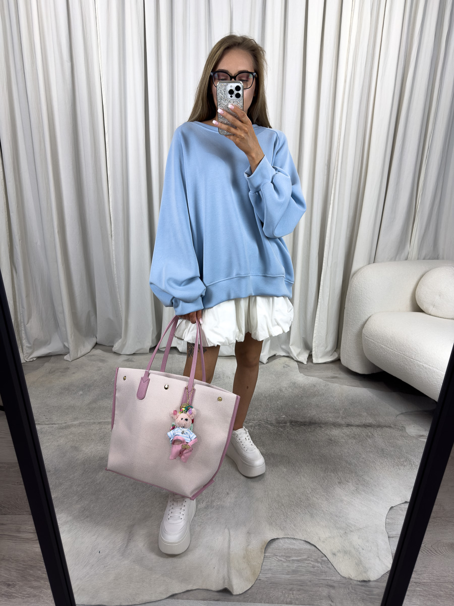 Modelka w błękitnej bluzie oversize Casual z plisowaną spódnicą i pastelową torbą, stylizacja streetwear z nutą dziewczęcości.