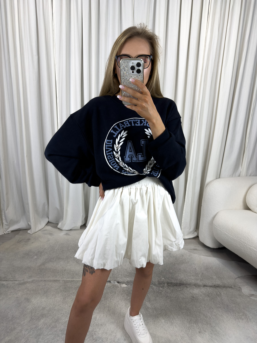 Modelka w białej mini spódnicy z popeliny Cutie o balonowym kroju i elastycznym pasie – stylizacja z bluzą oversize i sneakersami, zdjęcie produktowe na potrzeby sklepu internetowego.