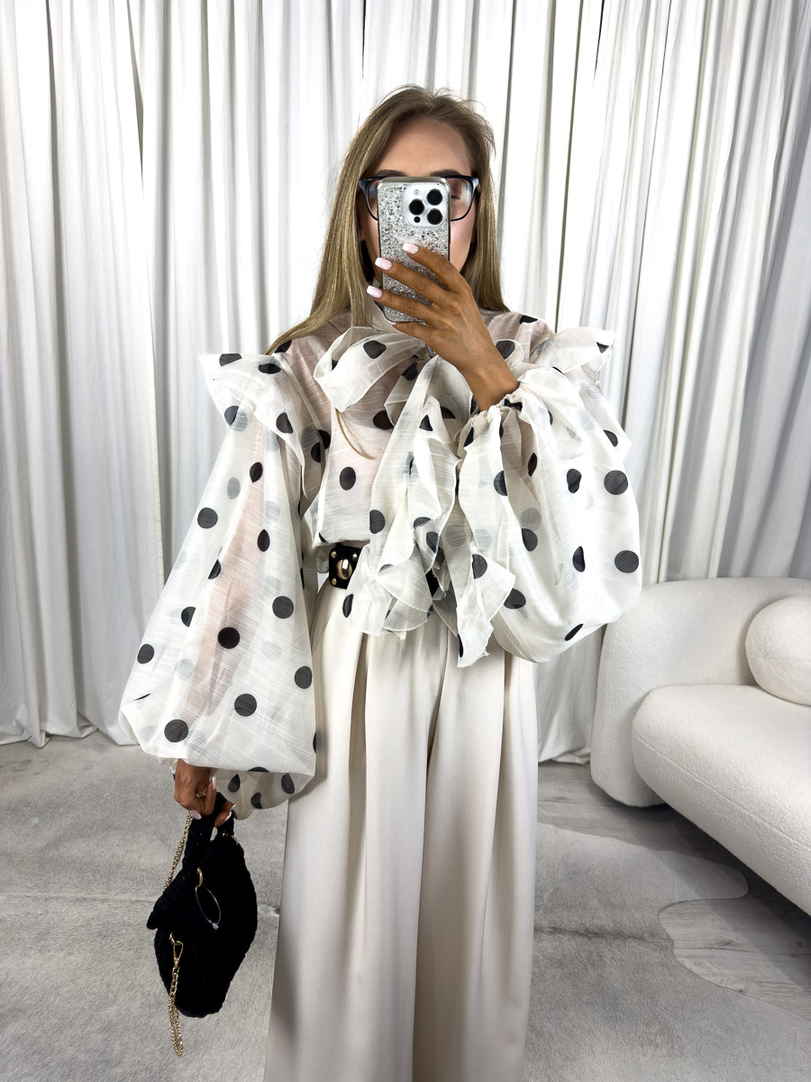 Modelka w koszuli oversize w grochy Sole z bufkami i kokardą pod szyją, połączona z szerokimi kremowymi spodniami i czarną torebką – zdjęcie produktowe do butiku internetowego.